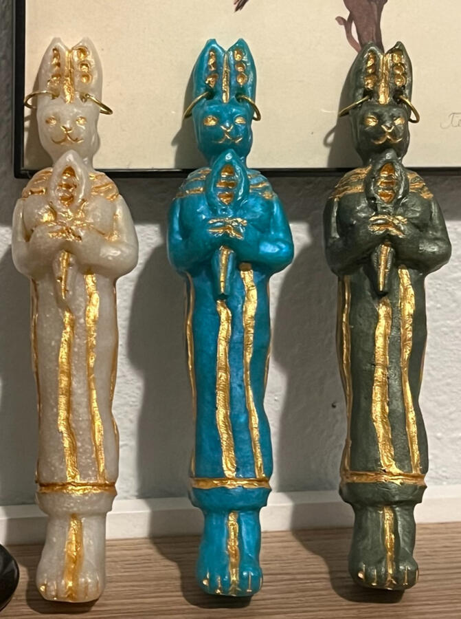 Hand-carved and hand-painted statuettes of the goddess Bast holding her sacred instrument, the sistrum, with her traditional golden earrings, designed to fit comfortable in your hand