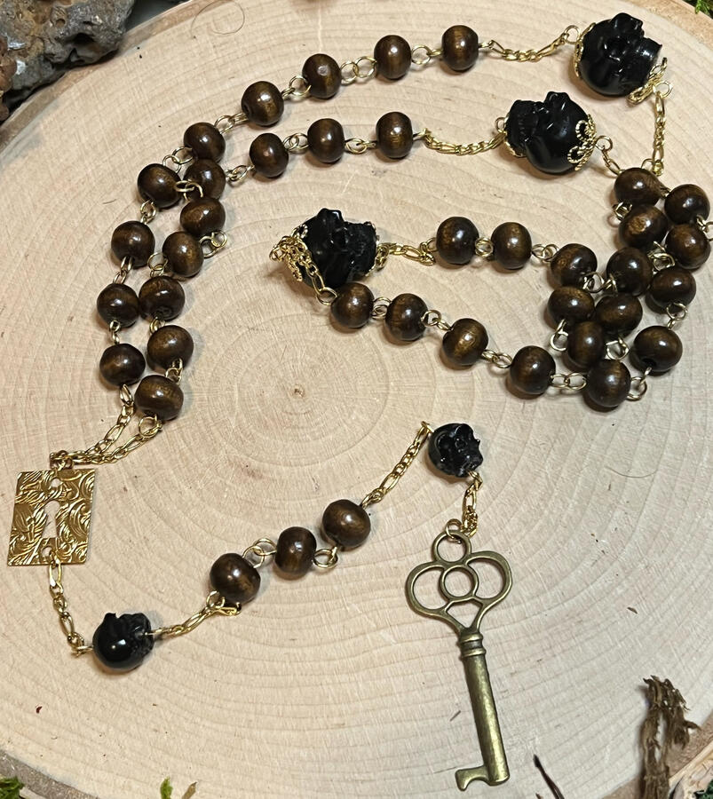 walnut wood beads, charcoal skull beads framed with gold filigree on the top and bottom, a swirling keyhole crosspiece, a skeleton key pendant