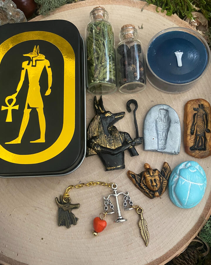 Travel altar to Anubis including: bottle of cypress, juniper berries, Anubis with crook altar tile, sarcophagus tile, Anubis hieroglyph, golden pharaoh, teal scarab, Anubis and Scales chaplet