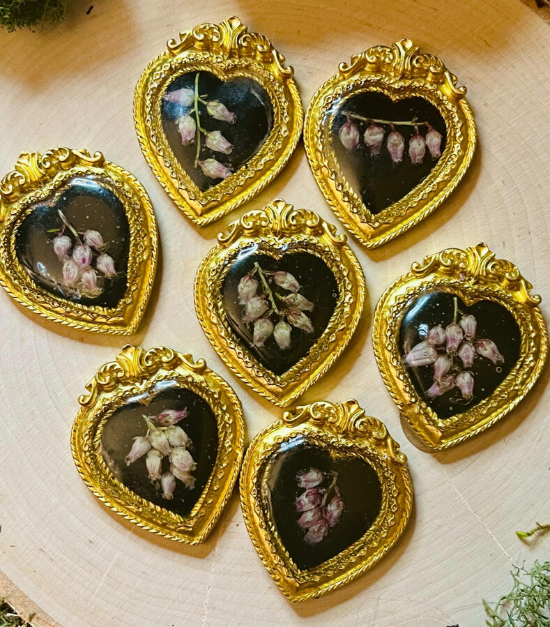 Floral altar tiles, with sustainably foraged flowers preserved on a black background in a golden heart shaped frame, created as offerings to the ancestors and graves to remember them by